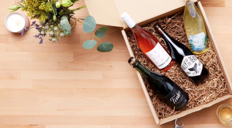 Wooden box with shredded paper and four bottles of different kinds of wine in it.
