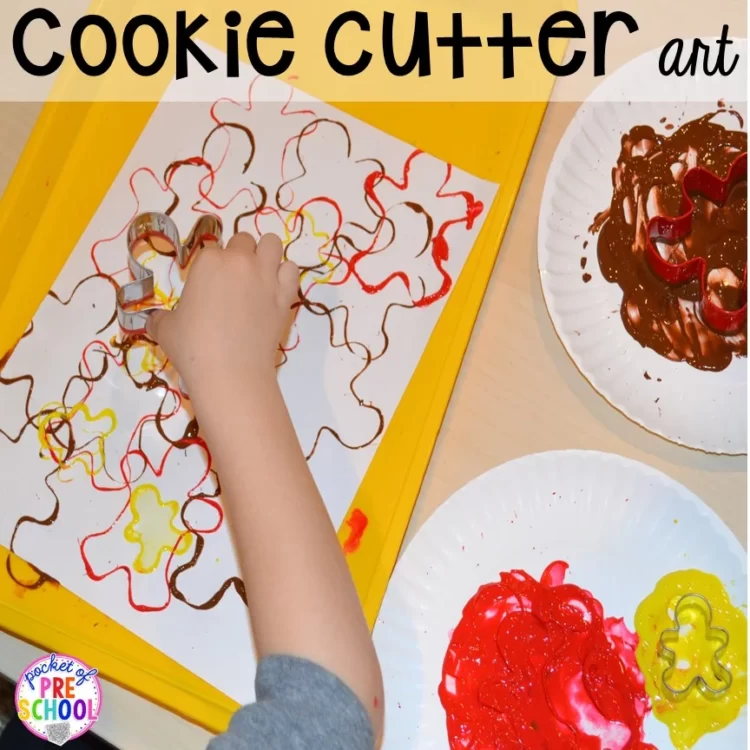 A child's hand using a gingerbread cookie cutter to paint on a piece of paper.