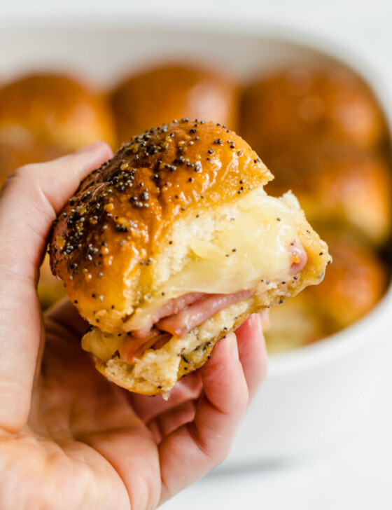 A hand holding ham and cheese sliders.