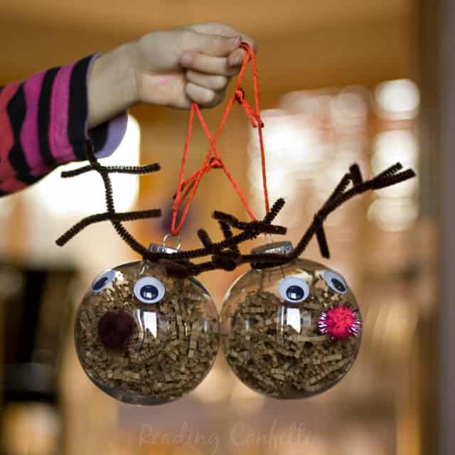 Two clear ornaments with shredded brown paper inside, googly eyes, pom pom noses, and brown pipe cleaner antlers.