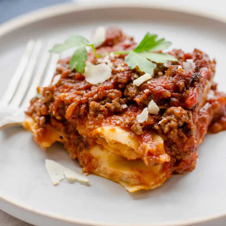 A serving of beefy baked ravioli on a plate with fresh parsley on top.