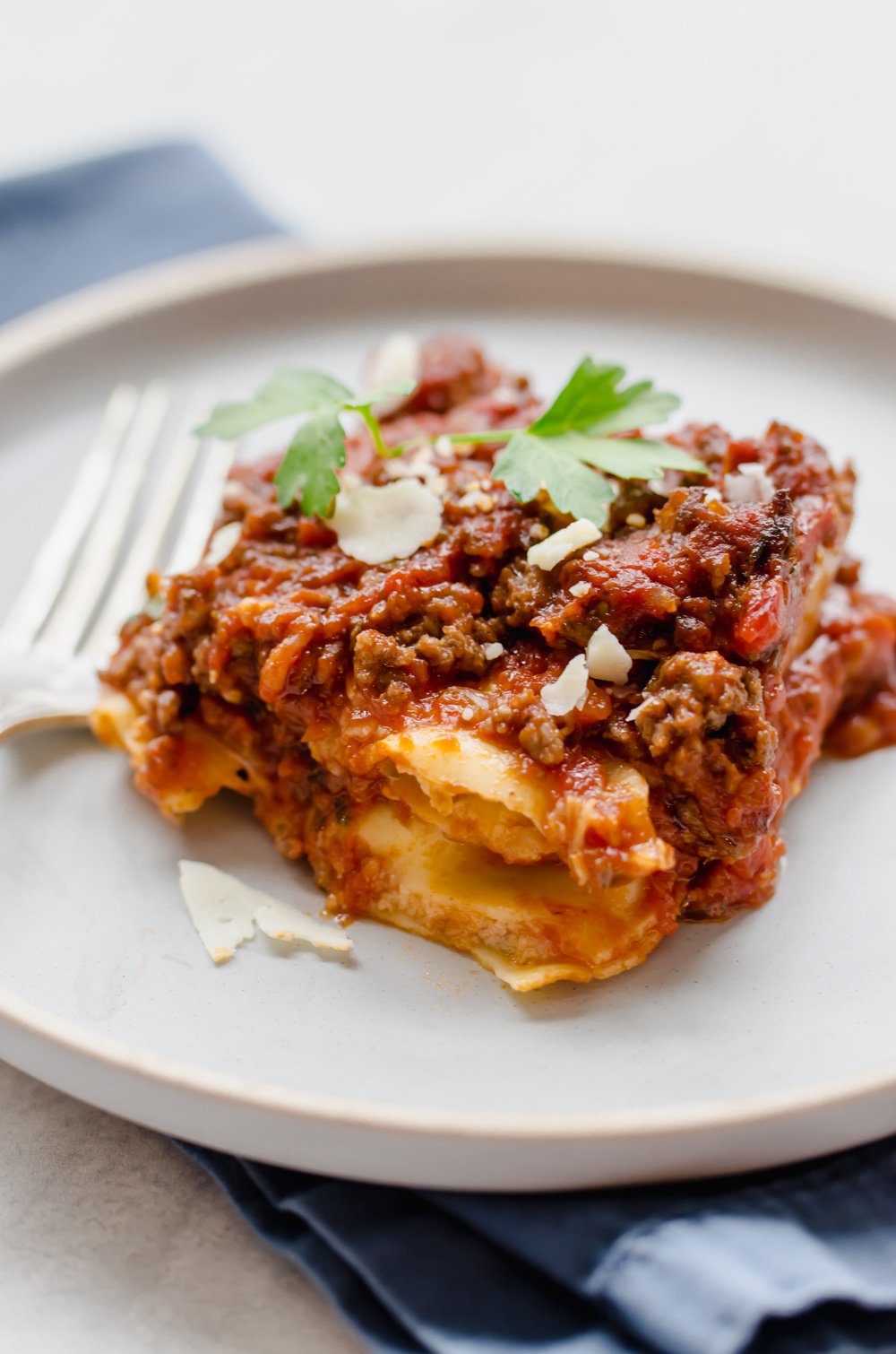 A serving of beefy baked ravioli on a plate with fresh parsley and shredded Parmesan on top.