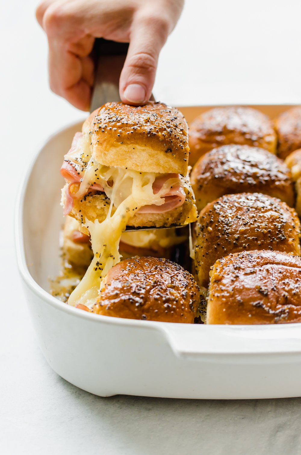 Ham and cheese sliders in a casserole dish with a spatula lifting one out to serve.