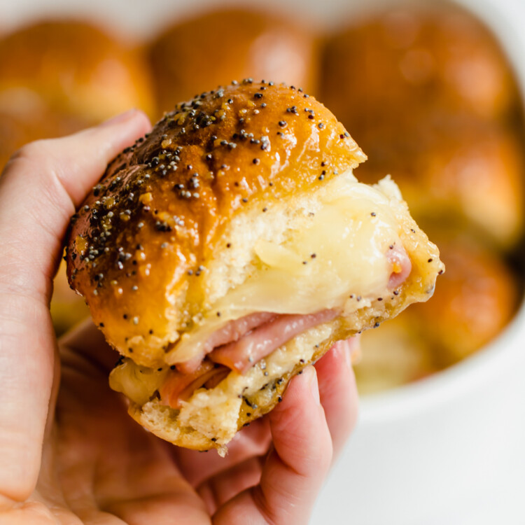 A hand holding ham and cheese sliders.