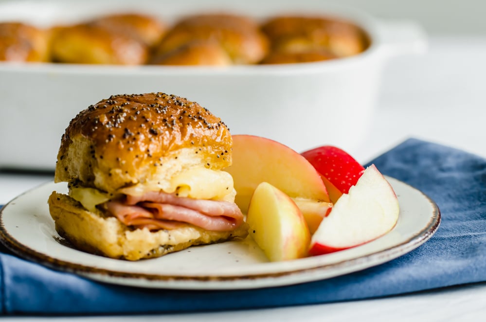 Ham and cheese sliders on a plate with apples.