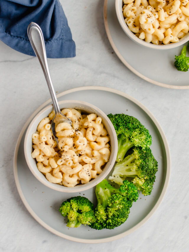 whole wheat mac and cheese in bowls on white plates with steamed broccoli on the side