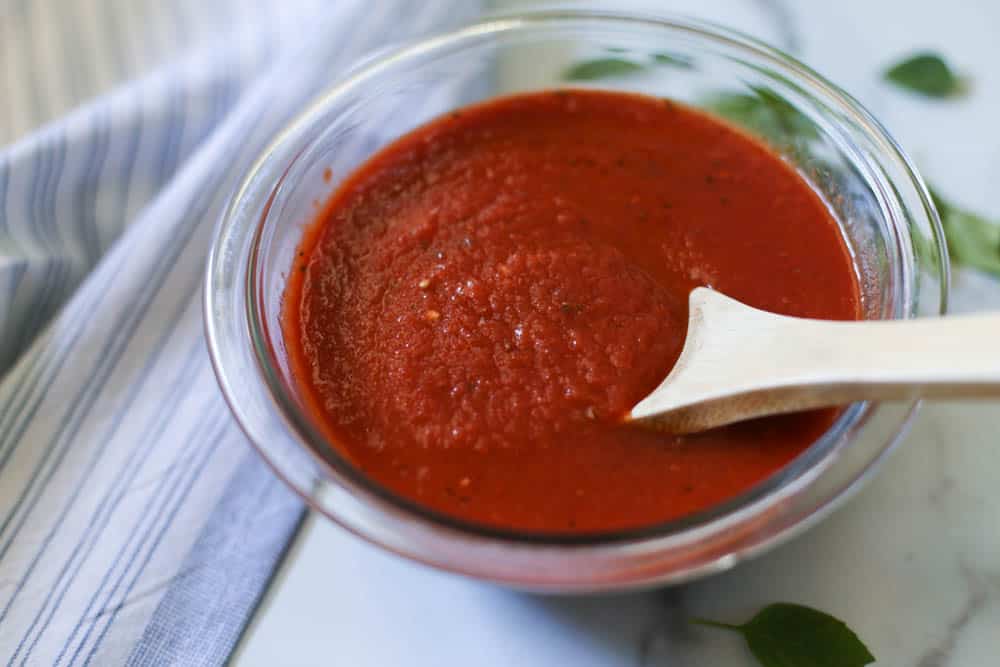 Freezer friendly sugar free pizza sauce in a glass bowl with a wooden spoon