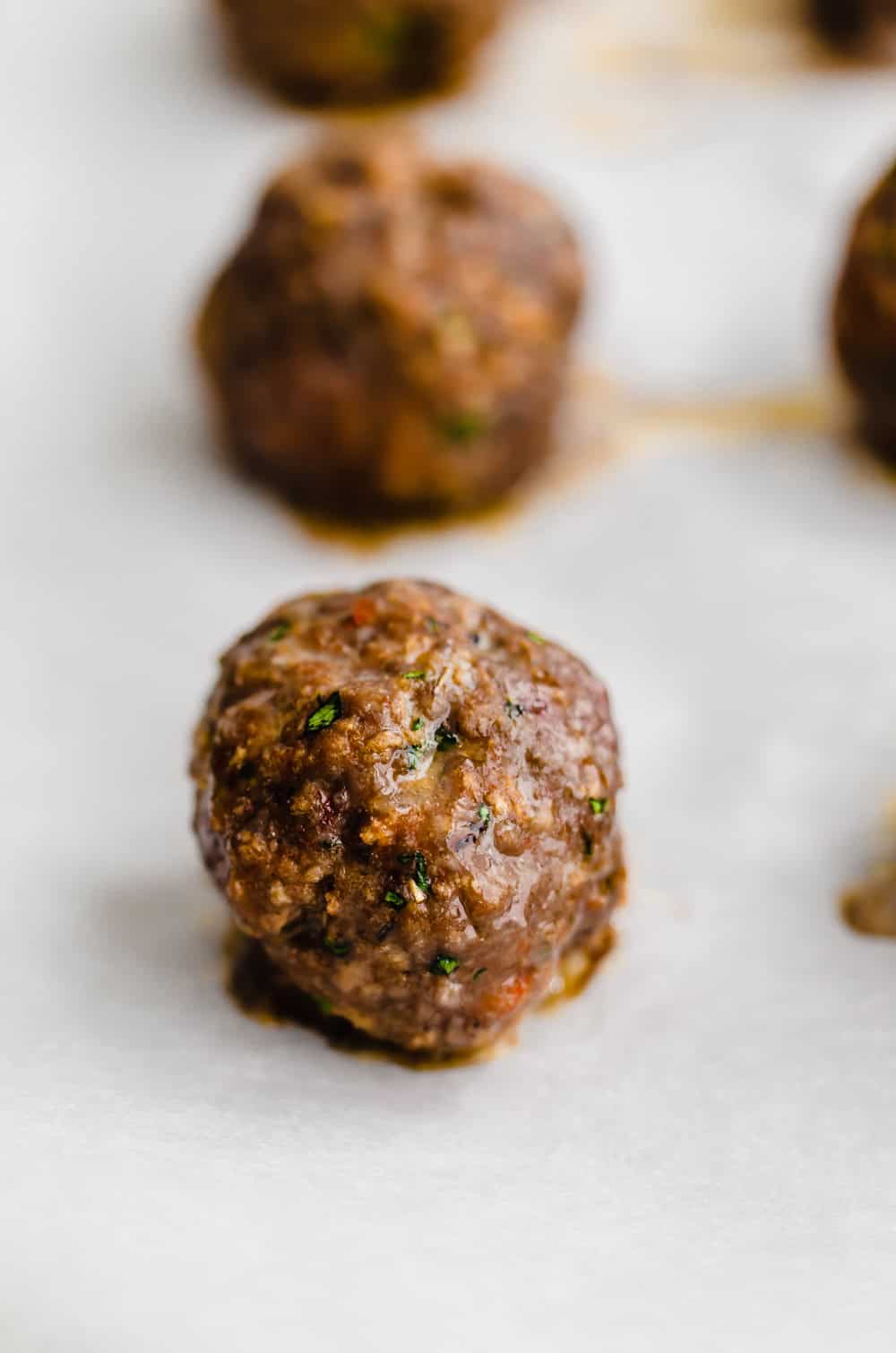 A baked Italian meatball colling on a sheet pan.