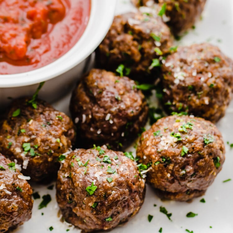 Baked Italian meatballs on a white platter with a small bowl of marinara sauce.