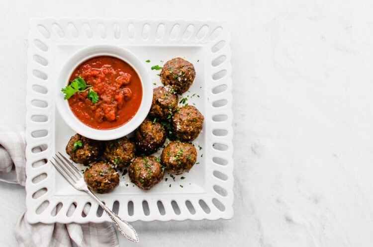 Italian meatballs on a white platter with a small bowl of marina sauce.
