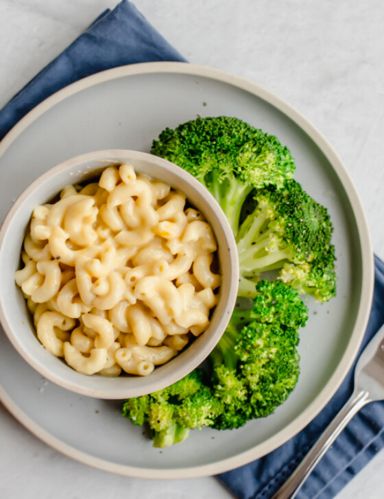 Mac and cheese in a bowl with steamed broccoli on the side.