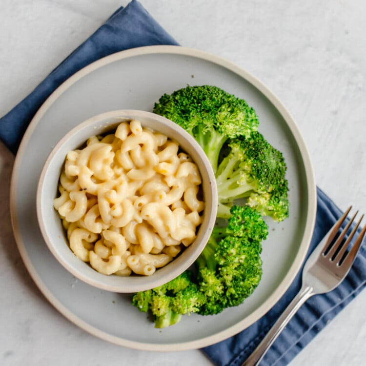 Mac and cheese in a bowl with steamed broccoli on the side.