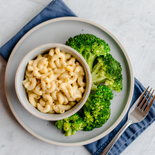 whole wheat mac and cheese in bowls on white plates with steamed broccoli on the side
