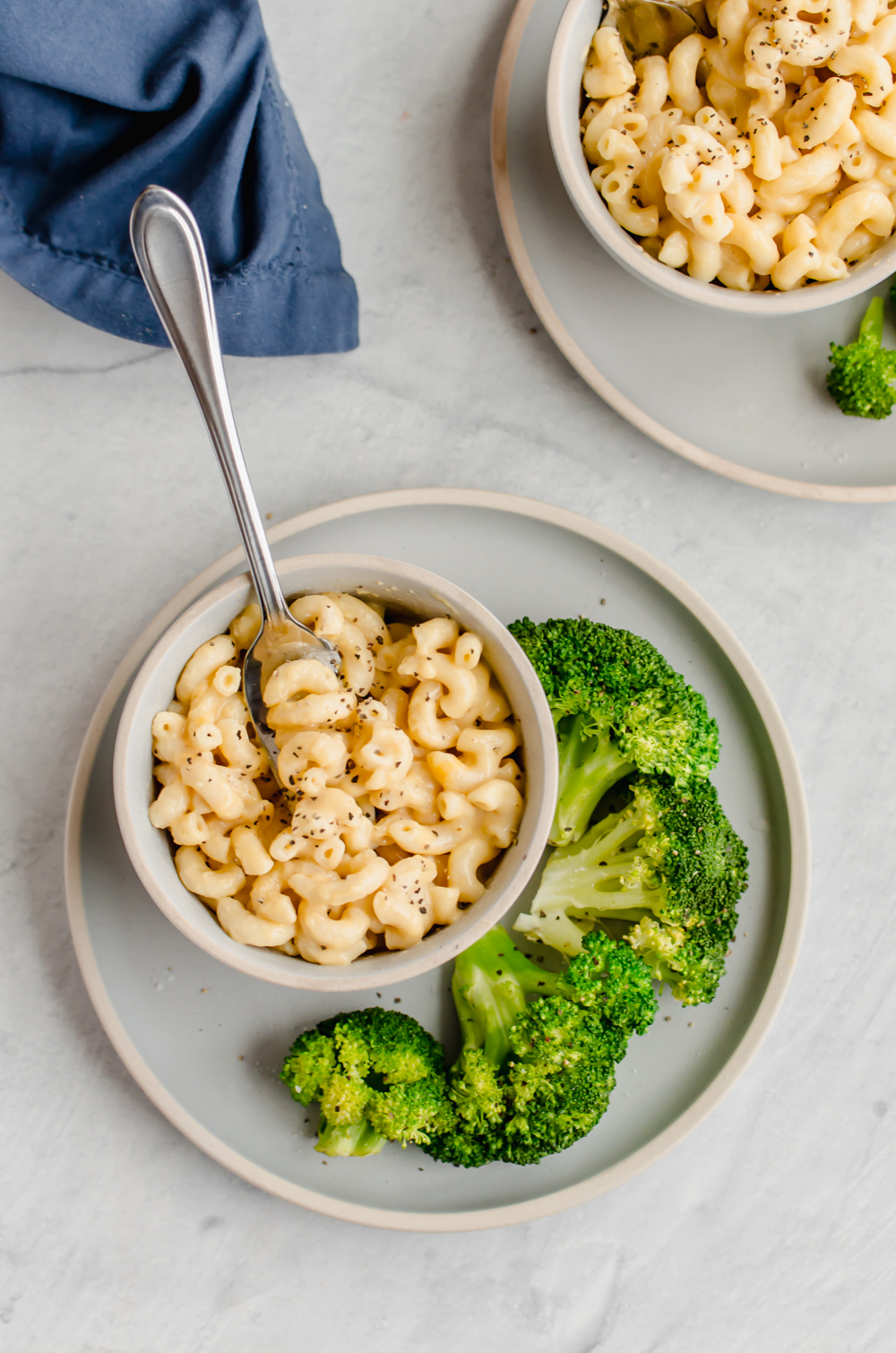 Two bowls of mac and cheese with sides of steamed broccoli.
