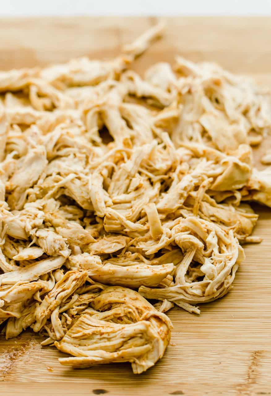 Shredded chicken on a wooden cutting board with taco seasoning on it.