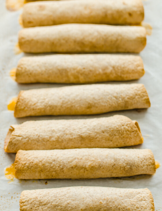 slow Cooker Chicken and Cheese Taquitos are rolled up and lined up on parchment paper.