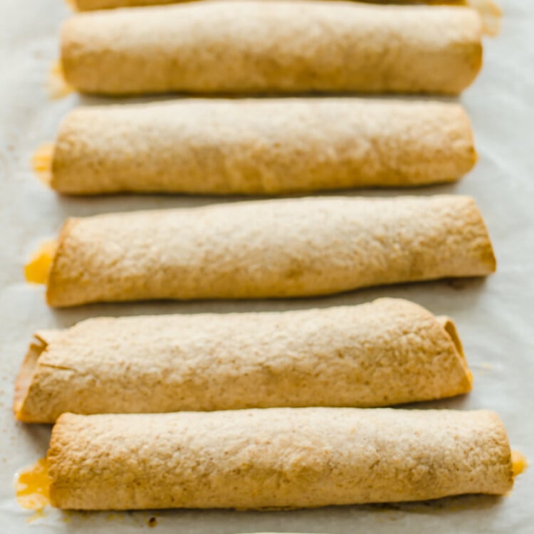 slow Cooker Chicken and Cheese Taquitos are rolled up and lined up on parchment paper.