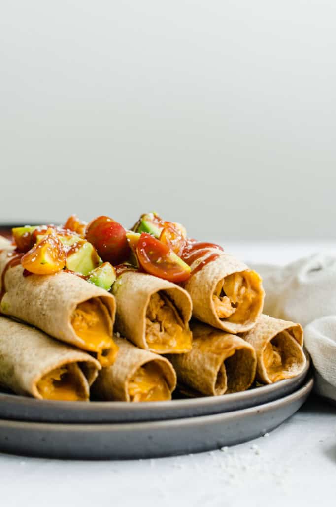 Chicken and Cheese Taquitos piled on a serving platter with avocado lime salsa on top