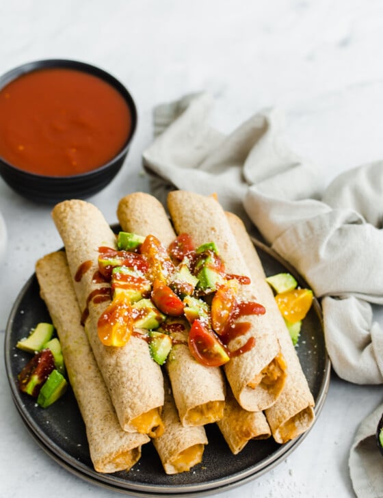Chicken and Cheese Taquitos piled on a serving platter with avocado lime salsa on top and salsa on the side.
