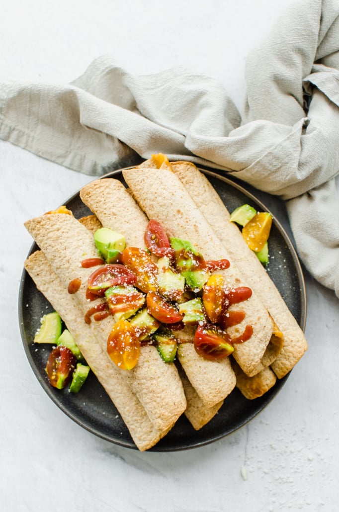 Chicken and Cheese Taquitos piled on a serving platter with avocado lime salsa on top