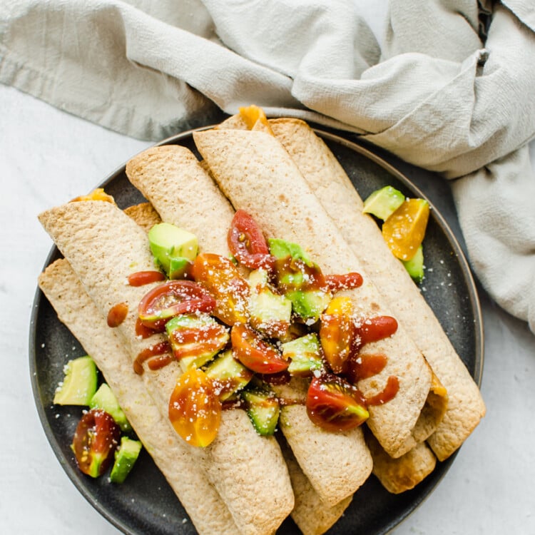 Chicken and Cheese Taquitos piled on a serving platter with avocado lime salsa on top.