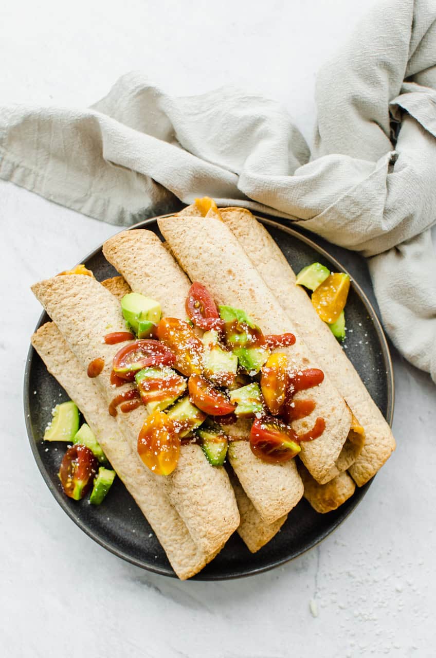 Chicken and Cheese Taquitos piled on a serving platter with avocado lime salsa on top.