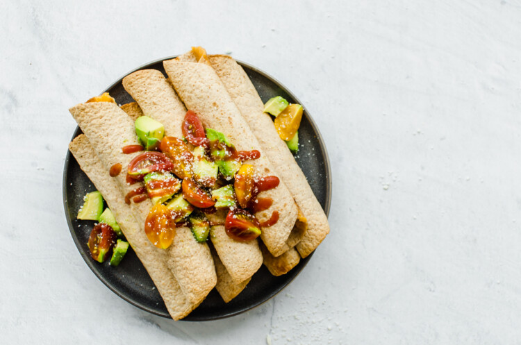Chicken Taquitos piled on a serving platter with avocado lime salsa on top.