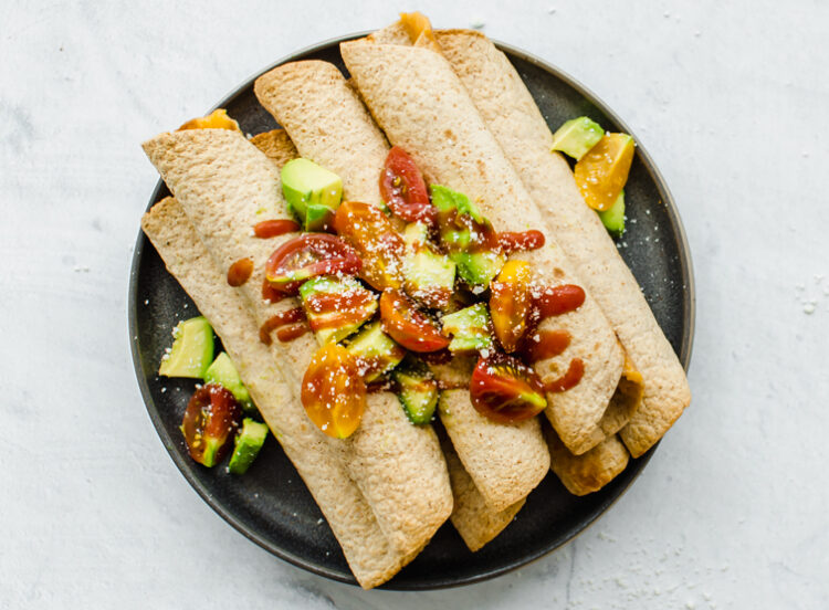Chicken Taquitos piled on a serving platter with avocado lime salsa on top.