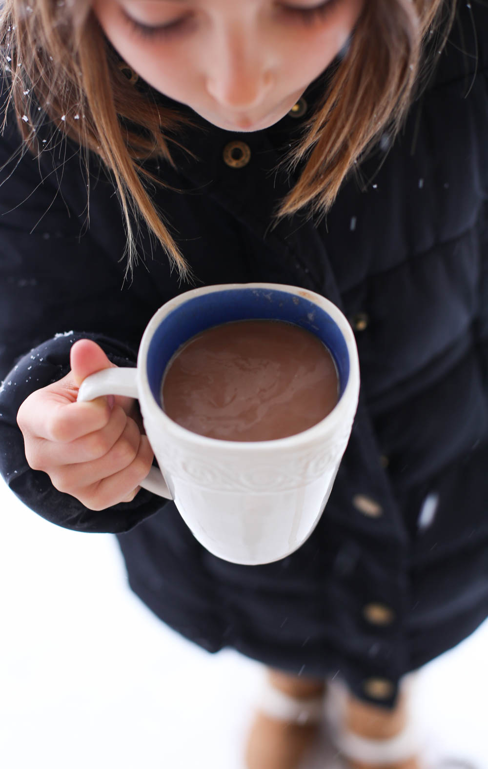 Young girl blowing on a mug of homemade hot chocolate.
