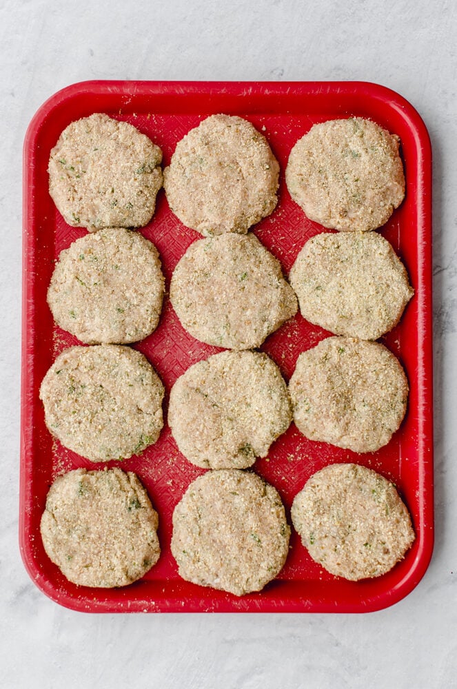 Chicken burgers prepped and on a red pan to be flash frozen.
