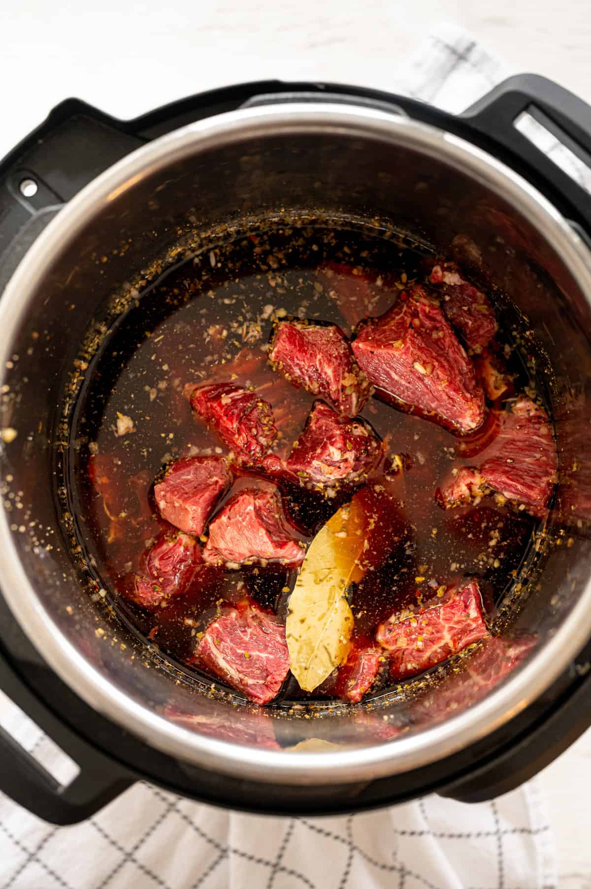 Raw chuck roast in 3-inch cubs with French dip ingredients in an Instant Pot.