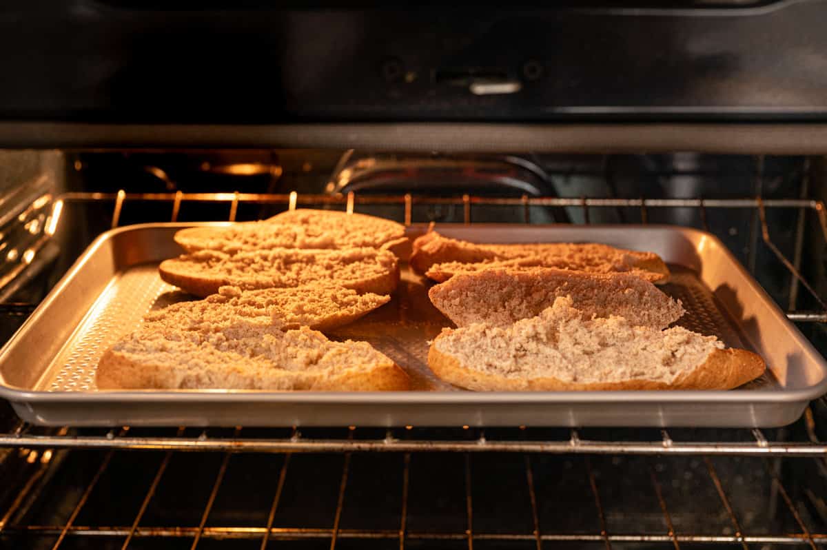 Open ciabatta rolls on a baking sheet under the broiler.