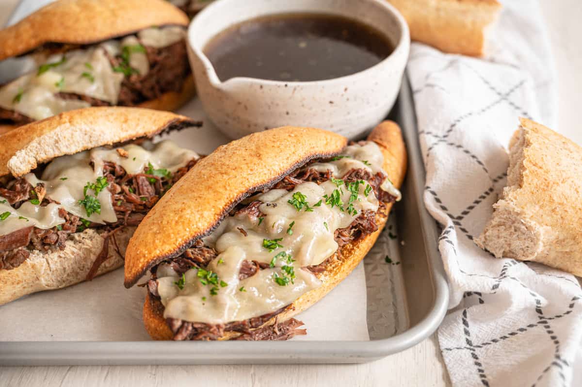 French dip sandwiches on a tray with au jus in a bowl.