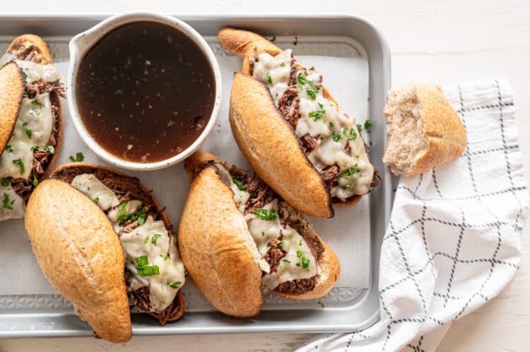 French dip sandwiches on a baking sheet with a crock of au jus.