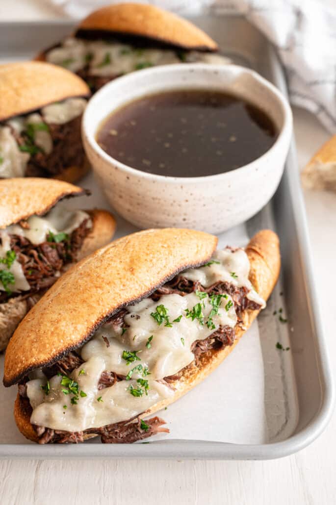 French dip sandwiches on a baking pan with a bowl of au jus.