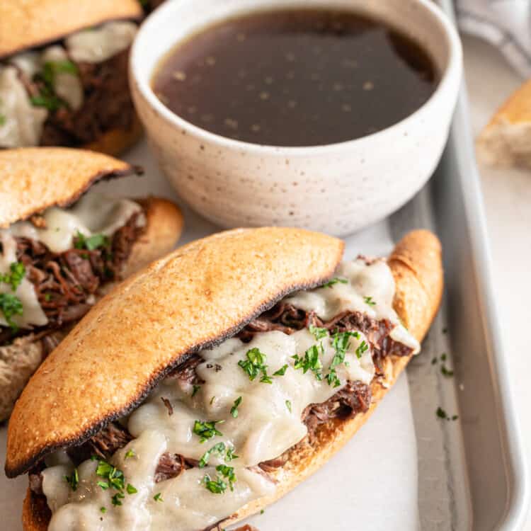 French dip sandwiches on a baking pan with a bowl of au jus.