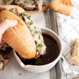 A French Dip sandwich being dipped in au jus sauce.