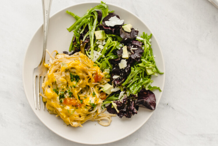 A serving of chicken spaghetti on a plate with a side salad.