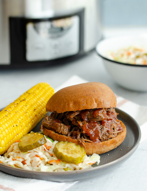 BBQ shredded beef on a bun with corn on the cob and coleslaw on a plate.