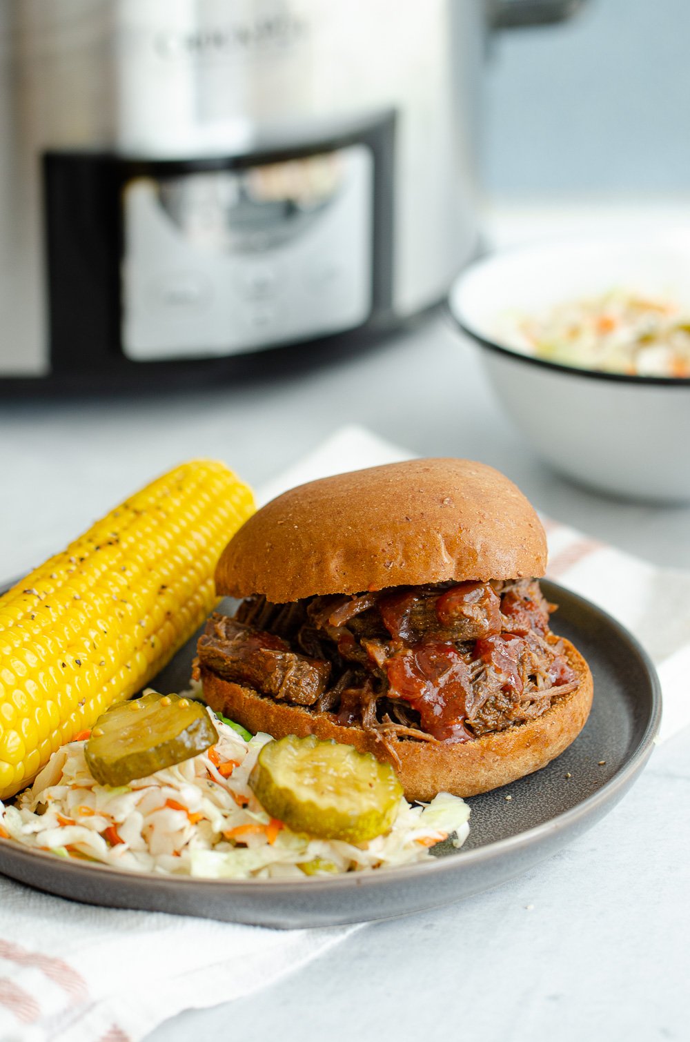 Slow Cooker BBQ shredded beef on a bun with corn on the cob.