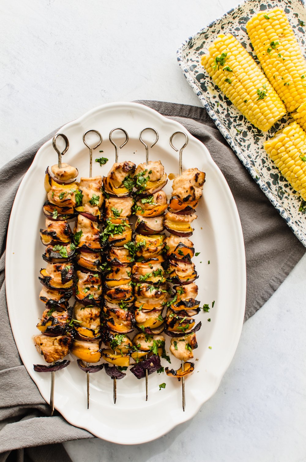 Grilled chicken kabobs with red onion and yellow peppers on a white platter.