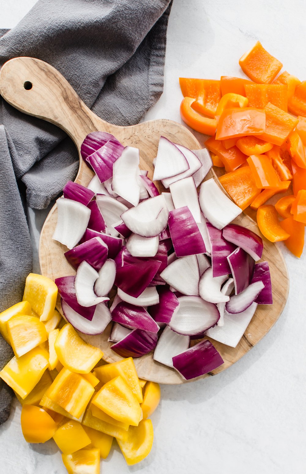 Chopped up red onion and bell peppers in piles on a small wooden cutting board.