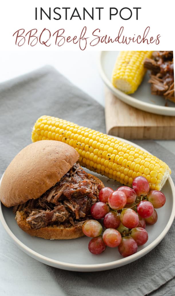 bbq shredded beef sandwich on a plate with corn and grapes