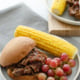 bbq shredded beef sandwich on a plate with corn and grapes