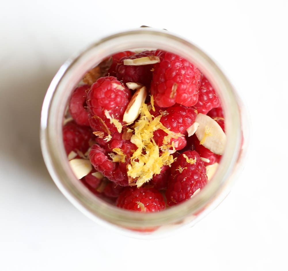 overhead shot of a mason jar with raspberries, lemon zest, and almond slices in it