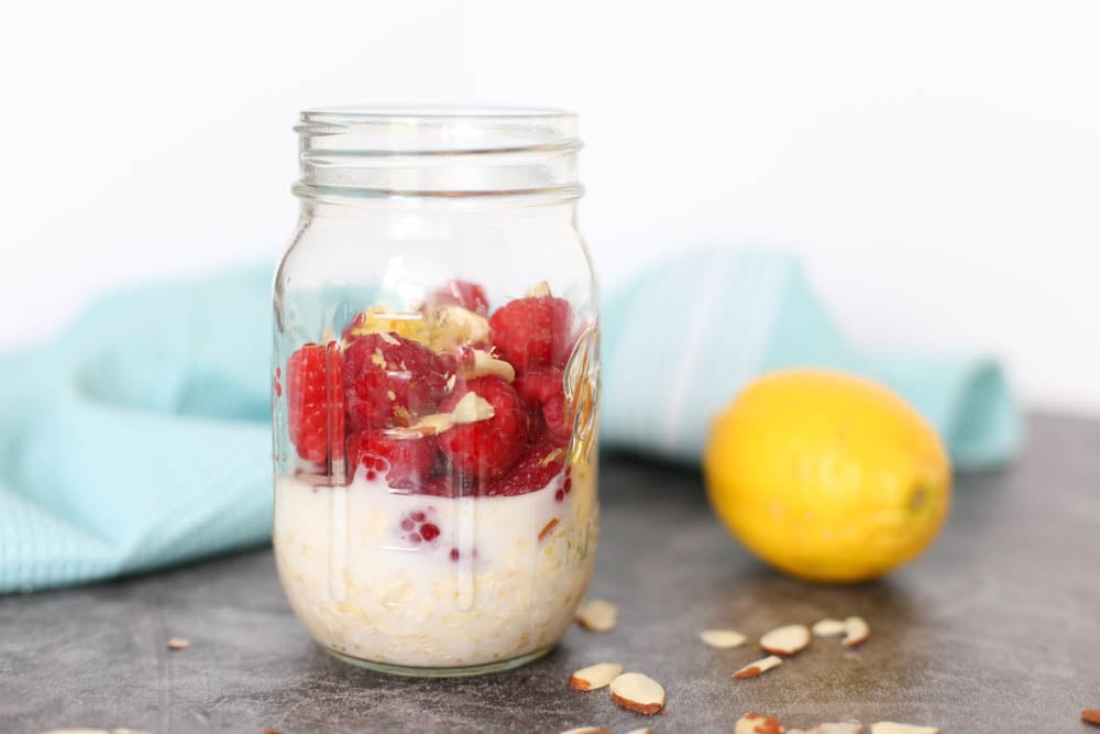 Raspberry Lemon Overnight Oats in a mason jar on a countertop with some sliced almonds on the counter and a whole lemon in the background.