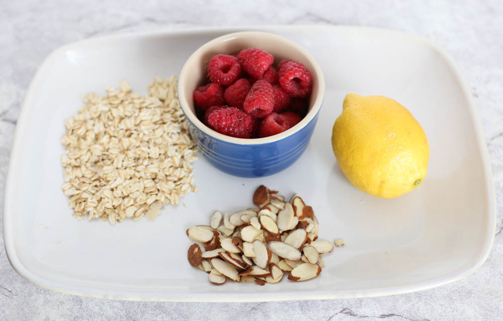rolled oats, raspberries, a lemon, and sliced almonds on a white plate