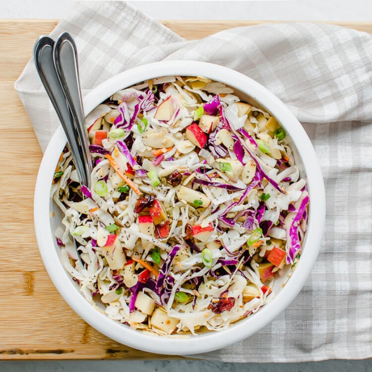 Asian slaw in a white bowl with spoons.