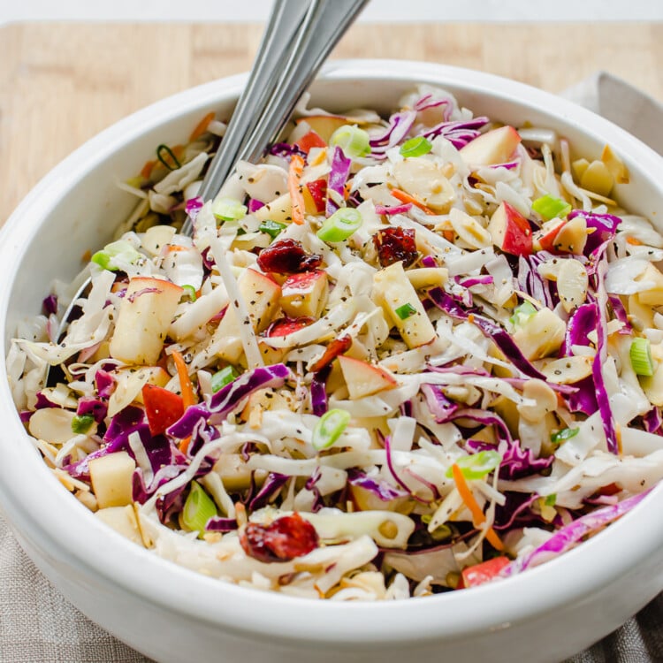 Asian slaw in a white bowl with spoons.
