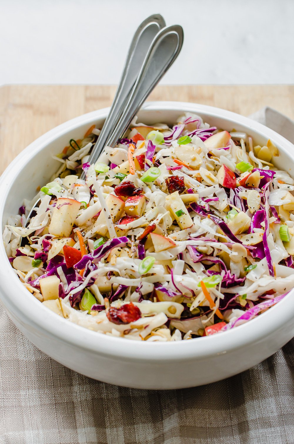 Asian Slaw in a white bowl with serving spoons in it.
